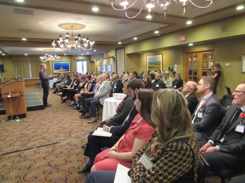 Man giving a presentation infront of a large group of people sitting down.