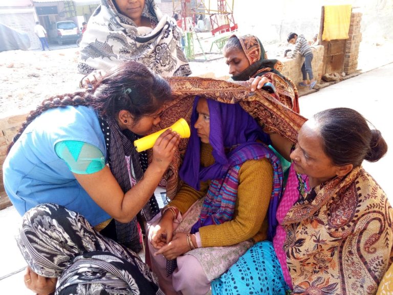 Eye screening being performed by a community health worker, woman holding a flashlight