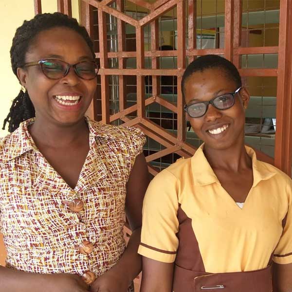 A young girl poses for a photo with her teacher. Both of them are wearing eyeglasses.