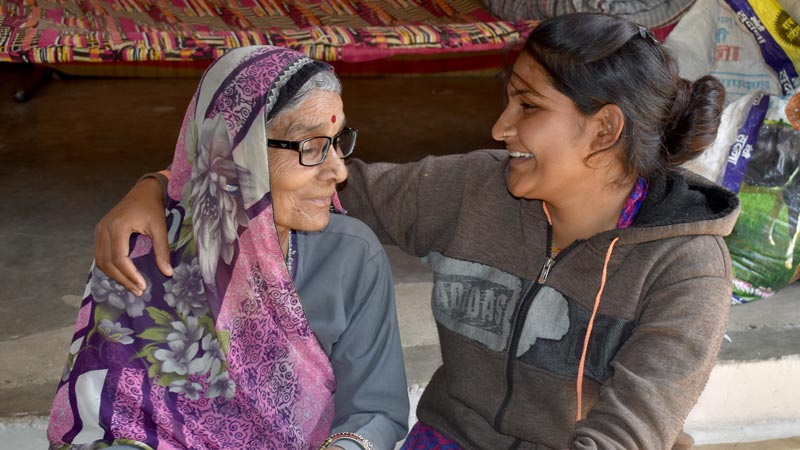 A young woman hugs and smiles at a senior woman wearing eyeglasses