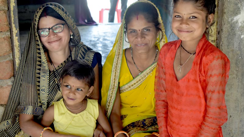 Two women, one of them wearing eyeglasses, sits with two children