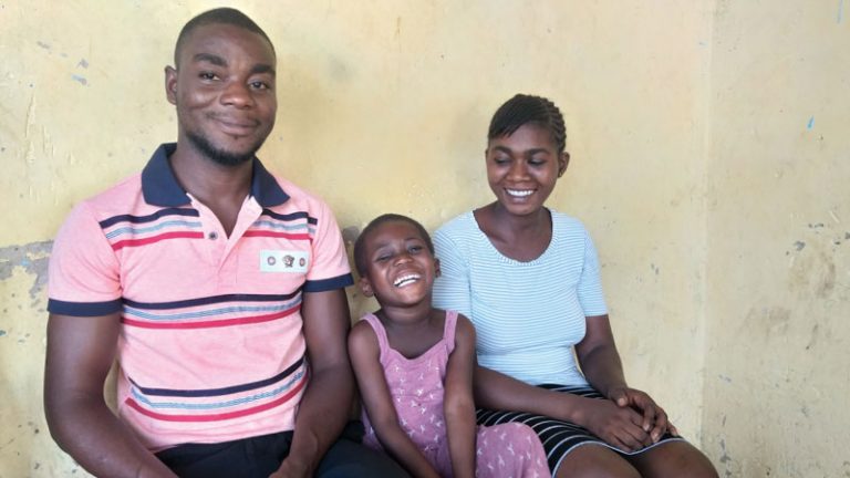 A young girl sits in between her parents smiling at the camera