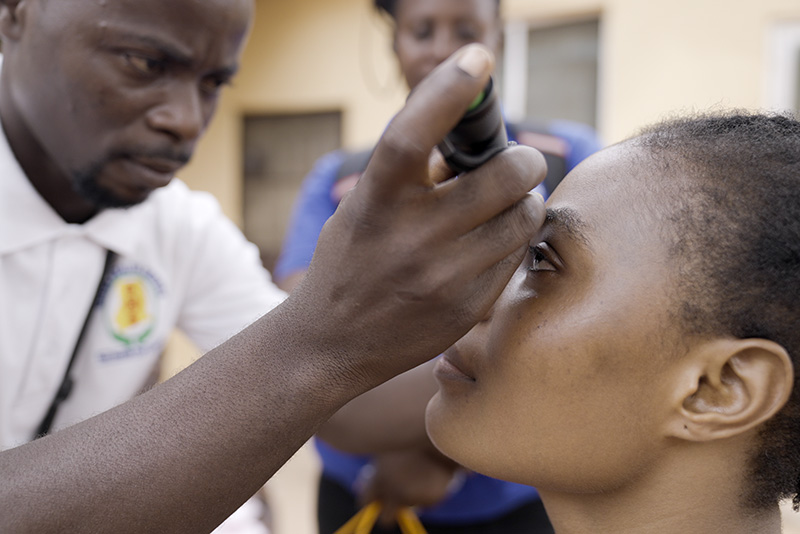 A healthcare worker uses a small, portable screening device to examine the eye of a female patient.