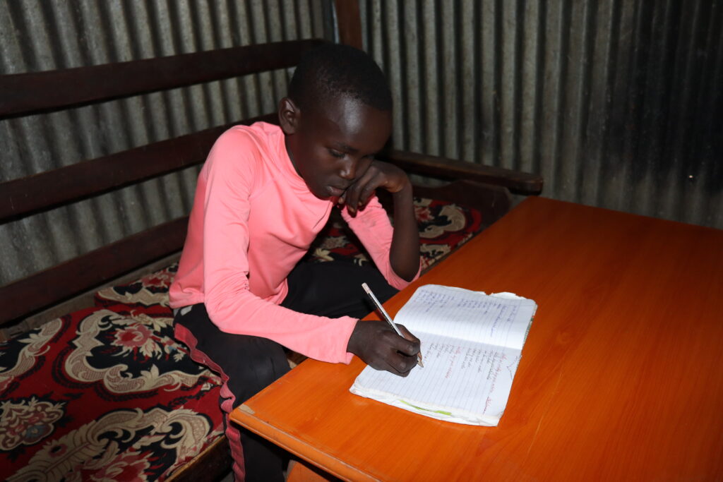 Young boy from Kenya sits at a table over a school workbook.