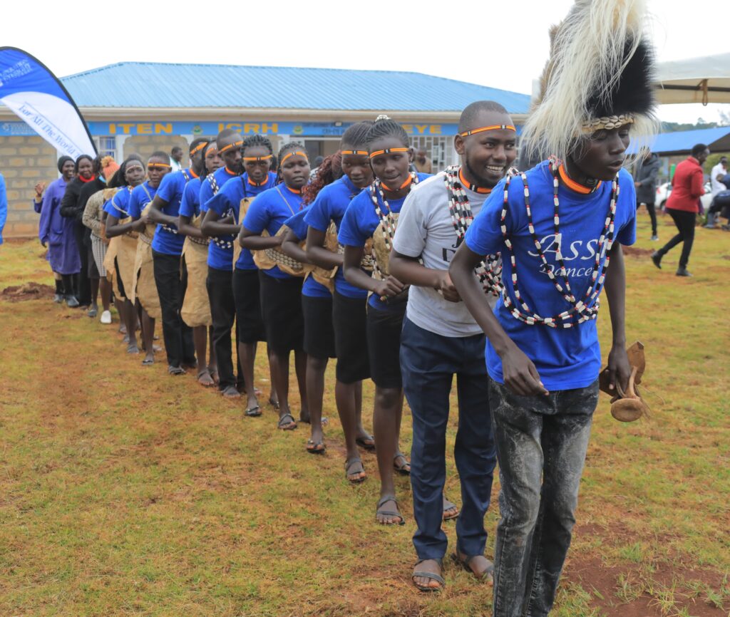 People line up in formation, dancing in front of a building with a blue roof.