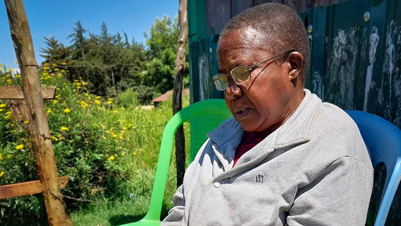 A woman wearing glasses sits outdoors in a blue chair.