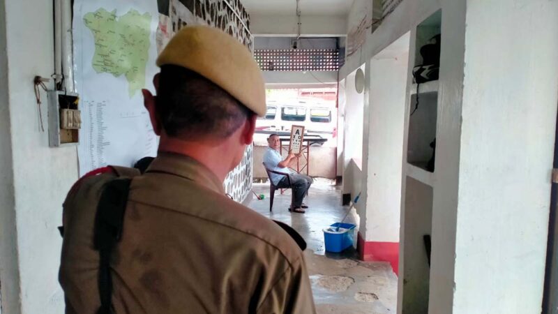 A police officer stands in the foreground, looking at an eye test chart featuring letters, in the background.