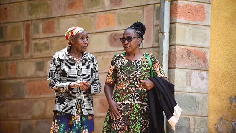 A female senior and a woman stand together outside a brick building.