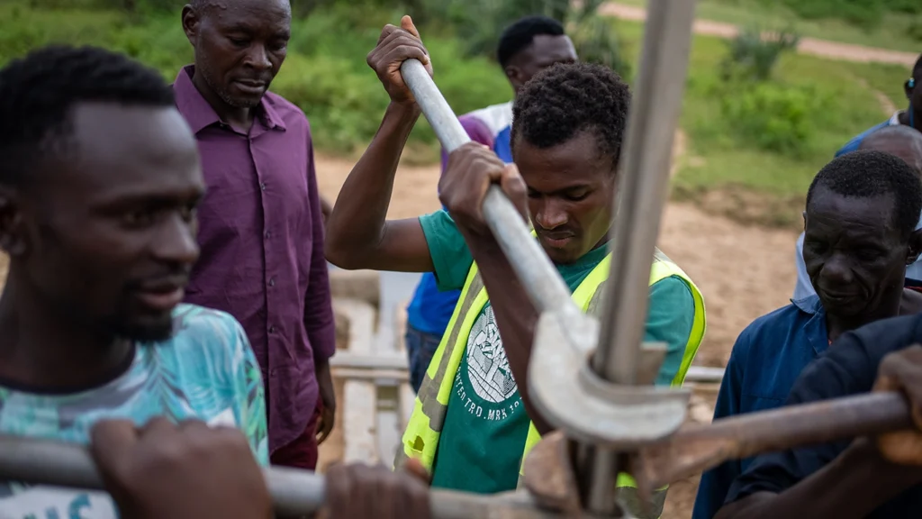 A group of men surround a pipe, using wrenches to turn it. 