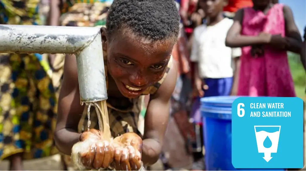A child washes her face at an outdoor water pump.