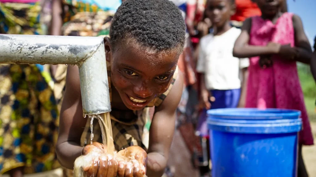 A girl washes her face at an outdoor tap.