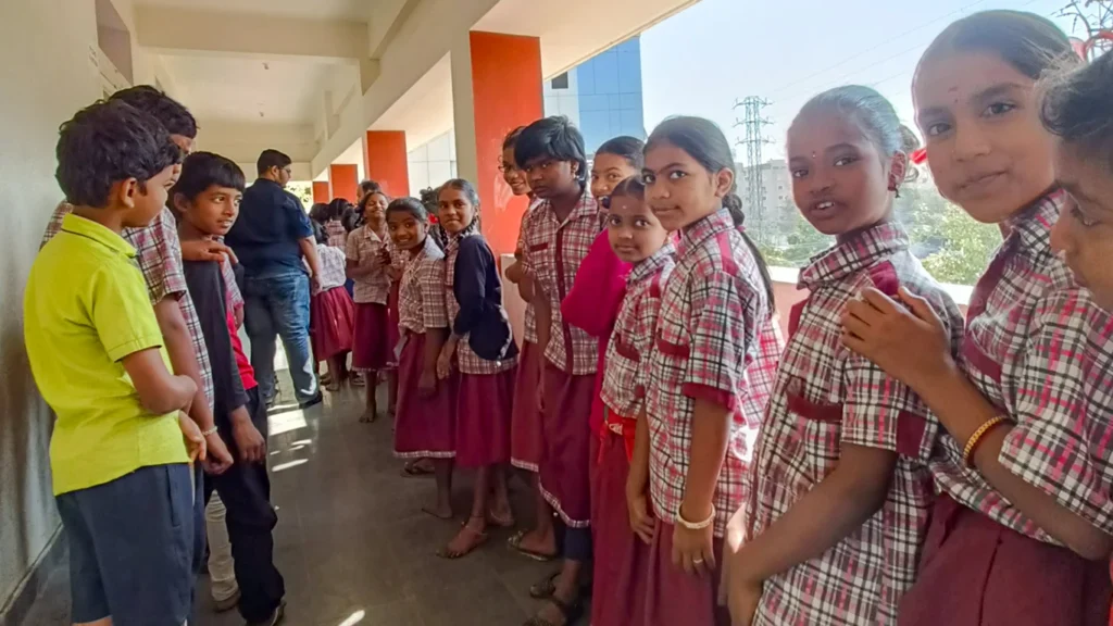 Students in uniforms stand in a queue in an outdoor school corridor.  