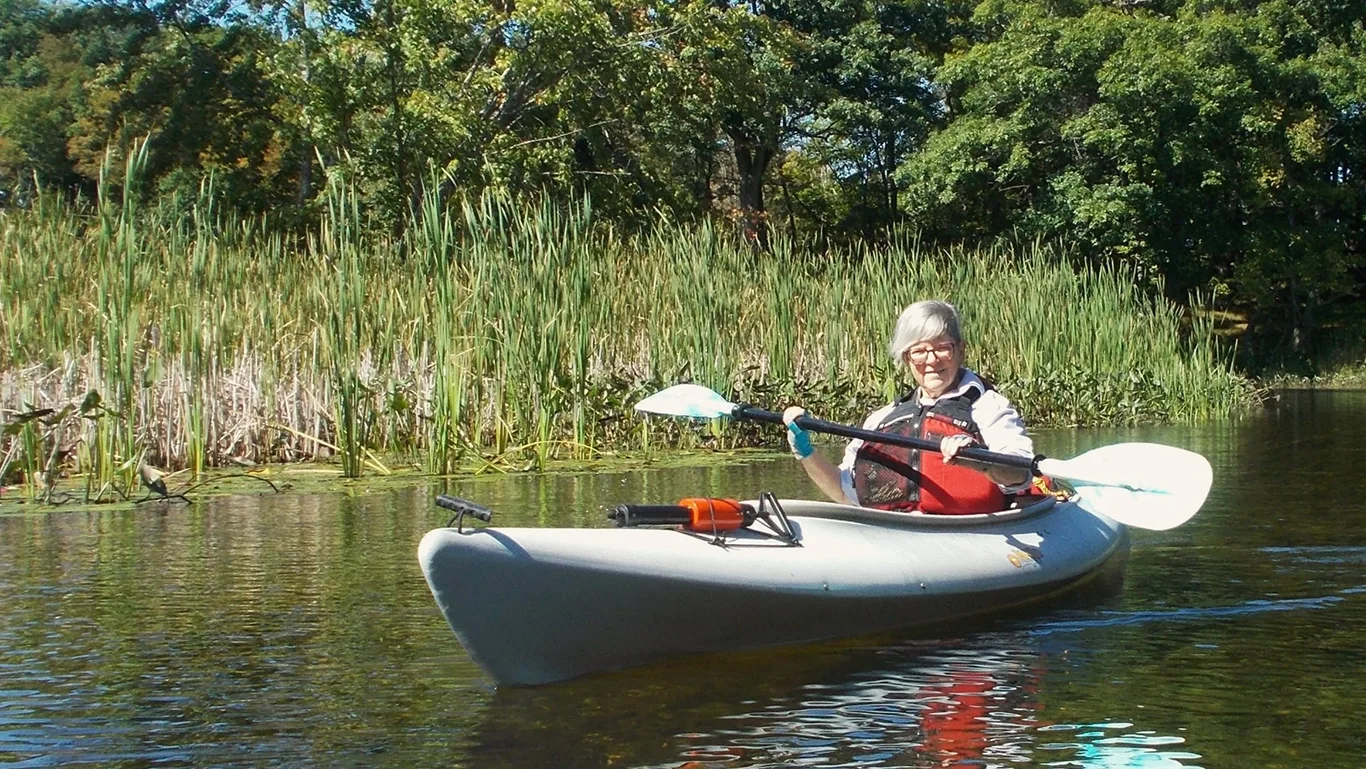 A woman paddles a kayak along a river.