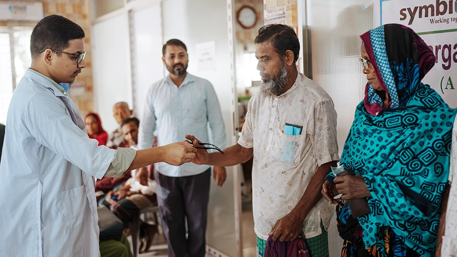 A man hands another man a pair of glasses, while a third man and a woman look on.