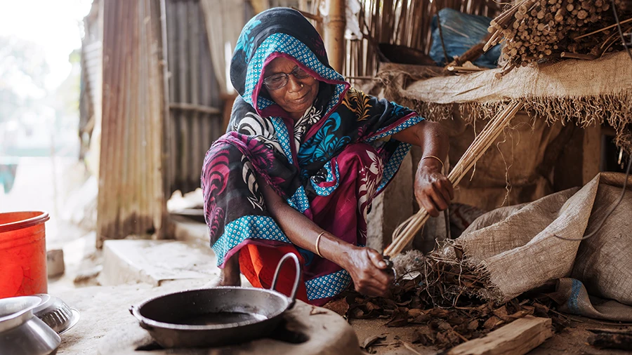 A woman sits in her kitchen lighting a cooking fire.