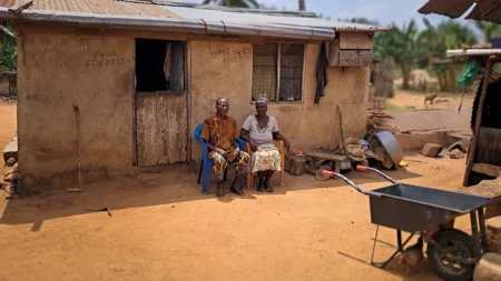 84-year-old man, Ayetu and his 75-year-old wife, Adwoa, smiling outside their home in their village, Adawukwa Fianko, Ghana.