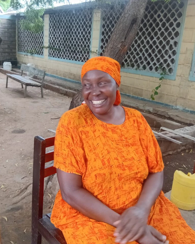 A woman wearing a bright orange dress and head wrap poses for the camera.