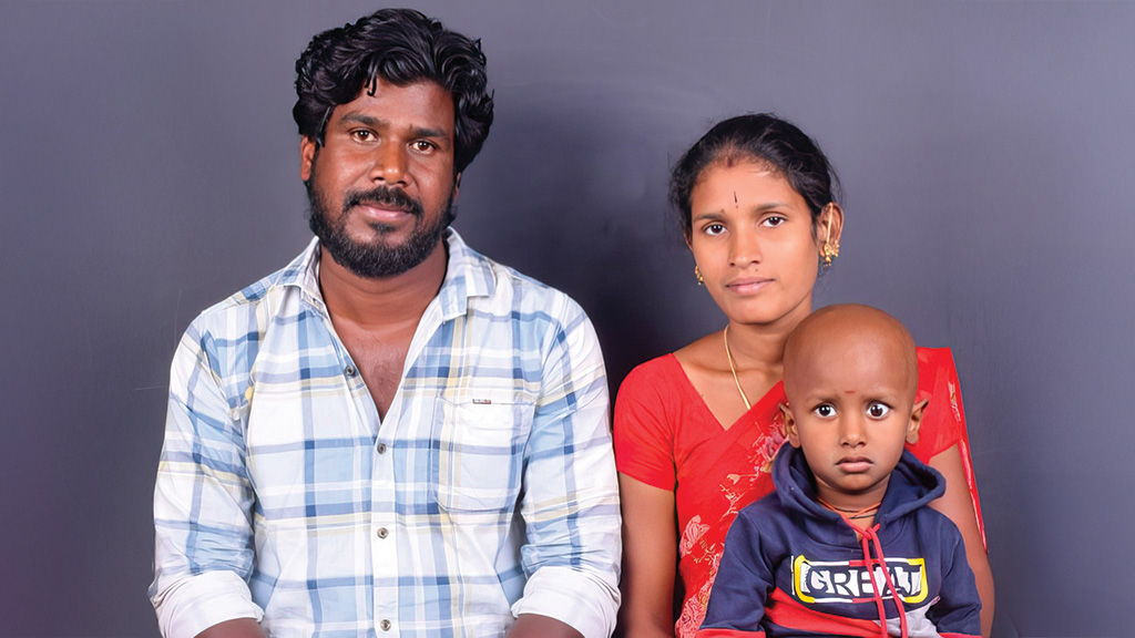 A mother, father and small child pose for a photo. The little boy has no hair.
