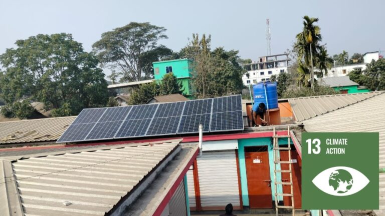A rooftop with a man sitting next to a solar panel array.
