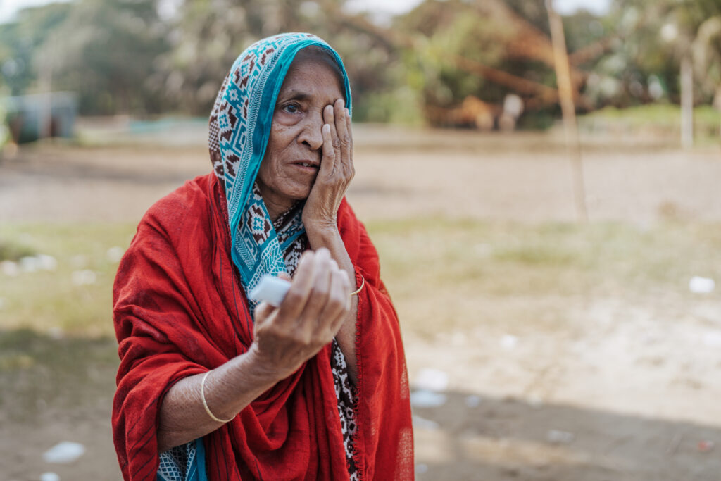 Gulbahar outside the Operation Eyesight outreach eye care camp. Here, she gently holds her left eye during a vision screening exam. After a thorough eye screening, she was referred to our partner, Symbiosis Hospital, for free cataract surgery.