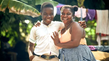A teenage boy and his mother stand close together smiling.
