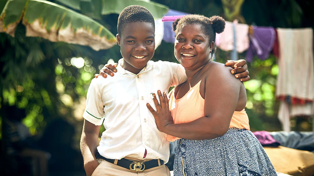 A teenage boy and his mother stand close together smiling.