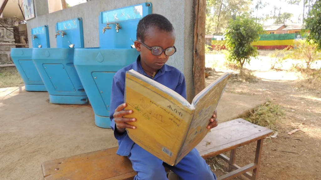  Fassikaw wearing glasses sits on the same bench, reading the book at a comfortable distance with improved posture and focus. 