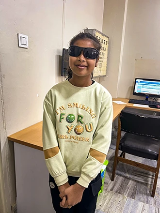 A girl stands in a clinic wearing a large pair of sunglasses. 