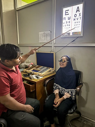A man points to an eye chart while a girl wearing optical trial frames looks on.